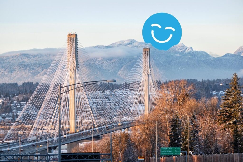 Vue d'un pont suspendu avec des montagnes en arrière-plan, entouré d'arbres. Un visage souriant bleu est superposé dans le ciel au-dessus du pont.