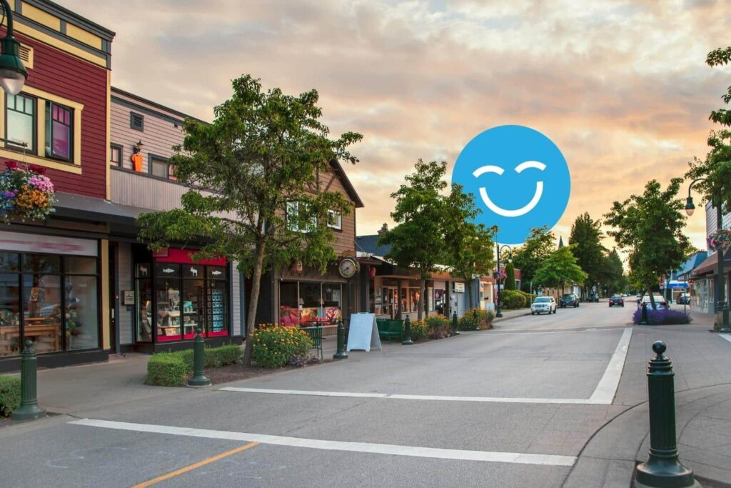 A quiet, tree-lined street with small shops under a sunset sky, featuring a superimposed blue smiley face in the sky.