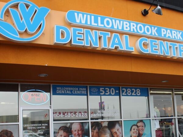 Signage for Willowbrook Park Dental Centre on an orange storefront, with window graphics featuring smiling individuals.