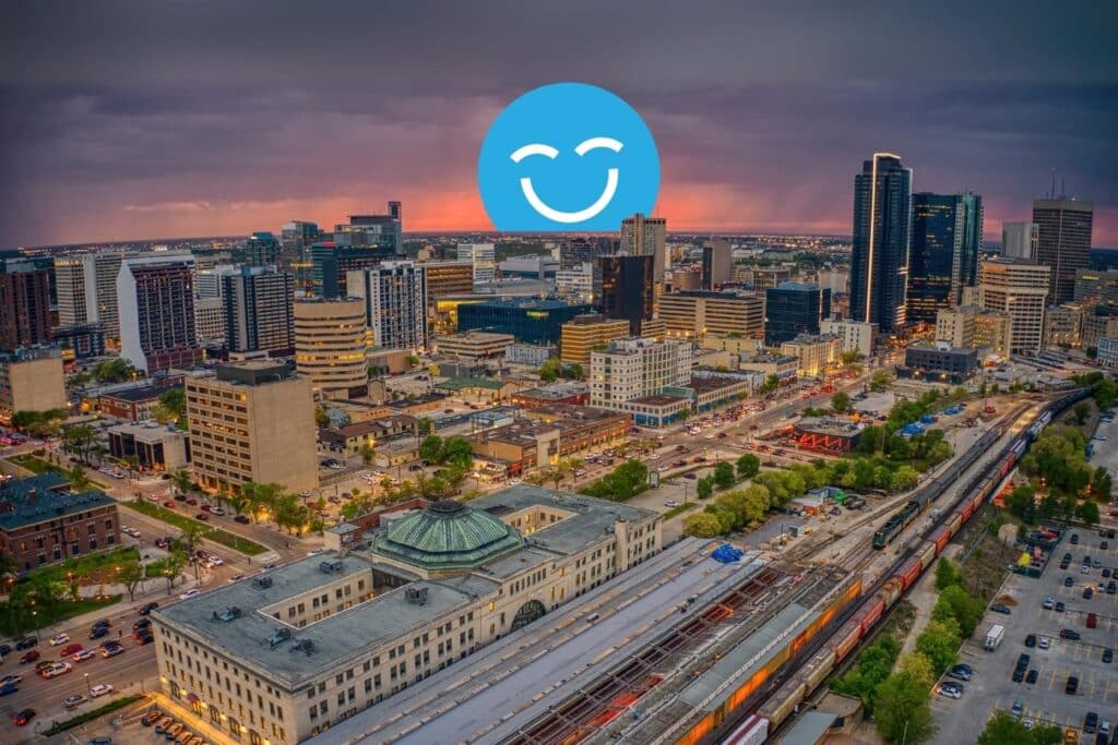 Aerial view of a cityscape at dusk with a train station in the foreground and skyscrapers against a dramatic, cloudy sunset sky.