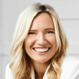 A woman with long blonde hair smiles brightly, showcasing her healthy teeth. She exhibits a warm and inviting demeanor, contributing to a friendly atmosphere.